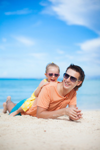 快乐的父亲和他可爱的小女儿躺在白色的沙滩上