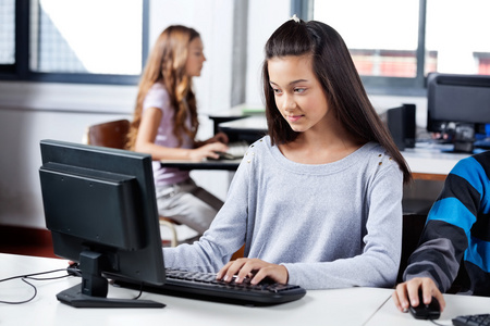 女孩与朋友在教室里使用计算机