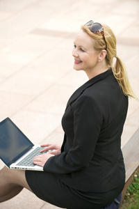 坐在户外用的笔记本电脑的开心事业女人