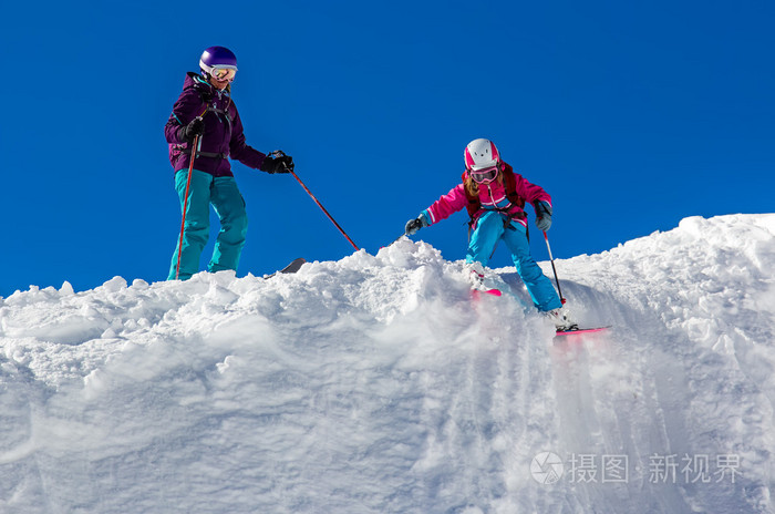 女孩与他的母亲在山陡峭的斜坡上滑雪