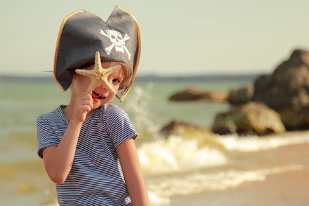 漂亮的小女孩在与控股在海滩上的海星骷髅海盗帽子