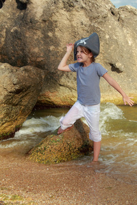 迷人的年轻女孩在海盗帽子站在海滩上水在夏季