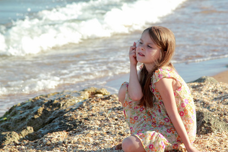 可爱的小女孩用微笑和持有贝壳梦肖像坐在夏天海的银行