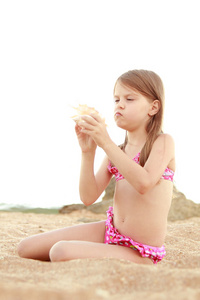 性格开朗的年轻美女坐在沙滩上和持有大贝壳