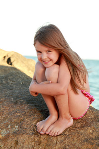 可爱的小女孩坐在海边的一块大石头上穿泳衣