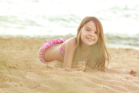 美丽微笑小女孩在粉红色泳装在海滩上的沙子被演奏