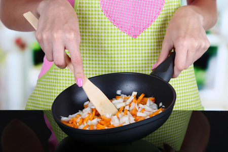 烹饪与泛在厨房里的胡萝卜炒的洋葱的手