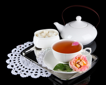 水壶和杯茶从茶玫瑰餐巾黑色背景上的金属托盘