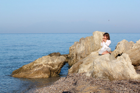 小女孩坐在海边岩石上和玩泛管