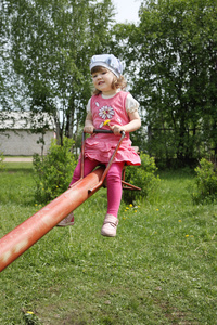 快乐粉红色的小可爱女孩骑上红跷跷板在夏季的一天