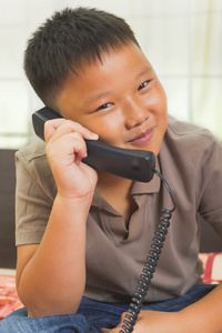 年轻的亚洲男孩看起来很开心在电话上