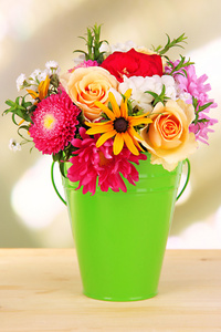 束美丽的鲜艳的花朵在彩色花瓶，木桌上，在明亮的背景上