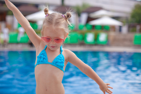 漂亮的小女孩张开双臂站在游泳池附近