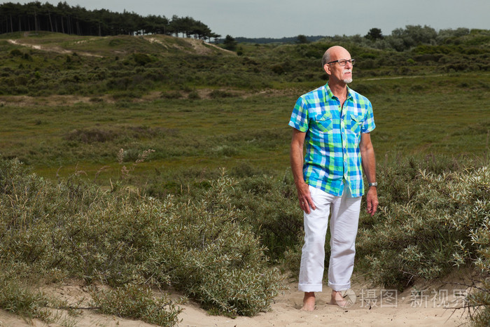 退休高级男人胡子和眼镜户外中草沙丘