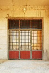 旧生锈车库门，涵盖的生锈的酒吧，粗糙的混凝土墙周围的玻璃