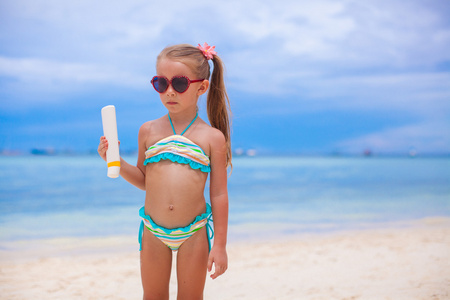 可爱的小女孩游泳衣持有防晒乳液瓶
