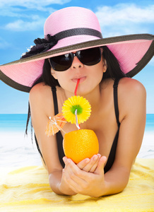 夏季度假女人躺在海滩黄砂毛巾微笑喝杯热带鸡尾酒