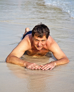 在 bathingsuit 中的男人是躺在沙滩上，享受 saltwa