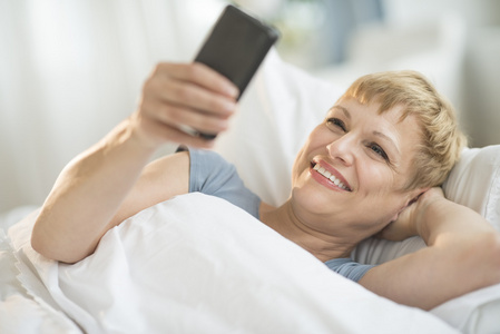 躺在床上时使用流动电话的女人