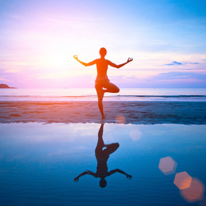日落时用反射水中练瑜伽在海滩上的年轻女子