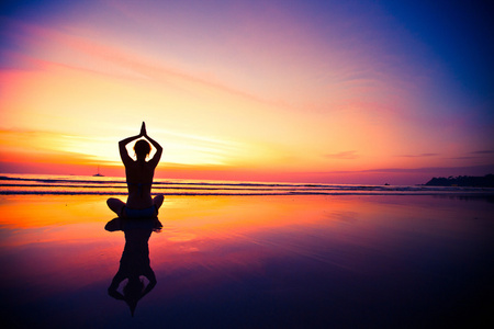 瑜伽女人坐在海岸上在日落时