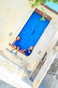 两个小可爱女孩坐在门前的台阶上的老房子在商场村 圣托里尼岛 希腊