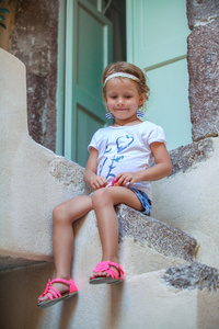 可爱的小女孩坐在台阶上，老房子在商场村 圣托里尼岛 希腊的
