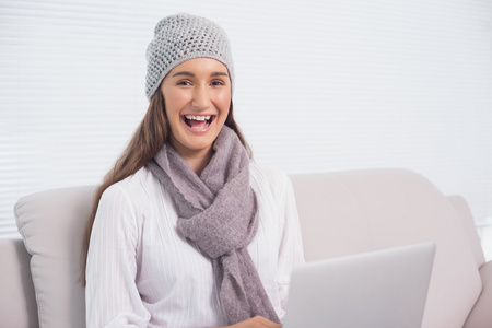 快乐的黑发女人冬季帽子上使用她的笔记本电脑