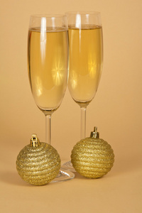 两个酒杯用香槟和米色背景上的两个金色新年的球