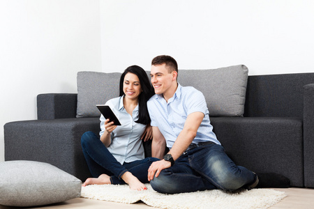 对年轻的夫妇快乐微笑在家里使用平板电脑触摸屏垫