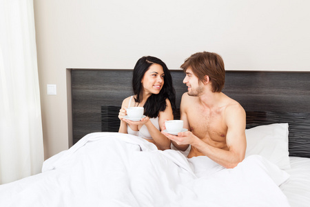 年轻的夫妇在床上喝咖啡