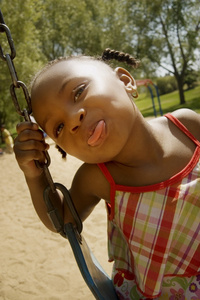 小女孩伸出她的舌头在公园的秋千上