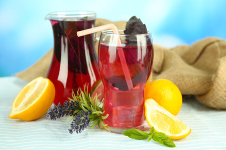 红罗勒柠檬水在水罐和玻璃 木桌上，在明亮的背景上