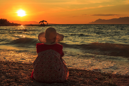 思维的女人坐在夕阳下海滩上