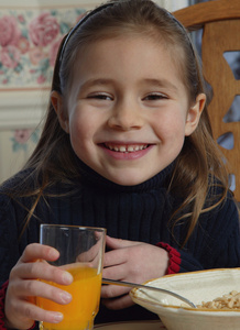 年轻的女孩，在早餐桌旁喝橙汁
