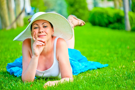 女孩躺在绿色的草坪，在一顶白色的帽子
