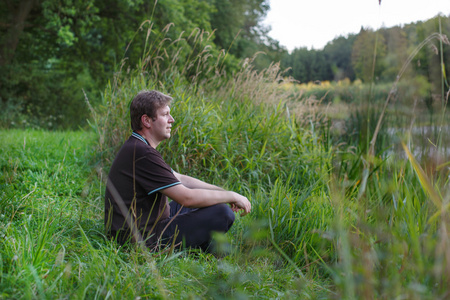 年轻英俊的男人坐在附近森林湖和放宽