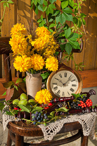 与古董时钟在阳光灿烂的日子仍然生活在旧木椅上的金球黄色的花朵花束