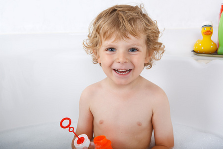 可爱的金发小孩男孩玩肥皂泡泡在浴缸里