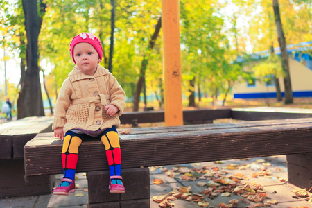 美丽的小女孩坐在长椅上在秋天公园