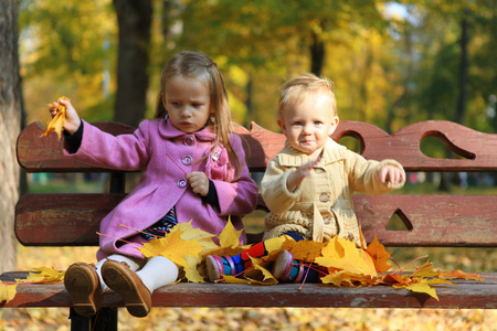 在温暖的秋天一天坐在长凳上的两个小的美丽女孩