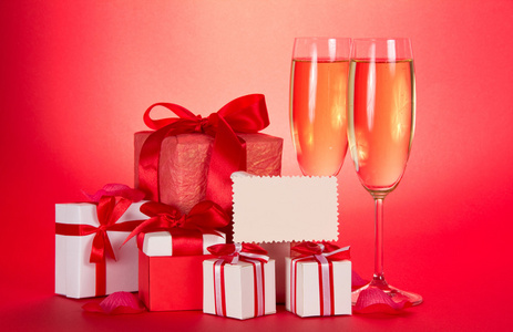 两杯香槟，礼品盒用磁带和弓箭 空卡和一个红色的背景上的花朵的花瓣