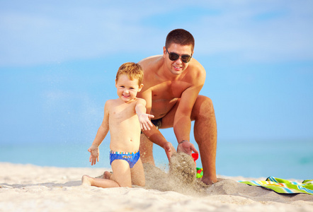 快乐的父亲和儿子在海滩上的沙子开心