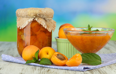 杏酱在玻璃罐和新鲜的杏子，木桌上，在明亮的背景上