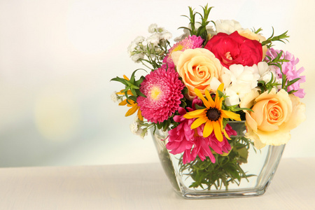 束美丽的鲜艳的花朵在玻璃花瓶，木桌上，在明亮的背景上