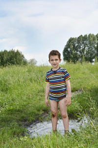 肮脏的乡下男孩光着脚站在水坑里.照片