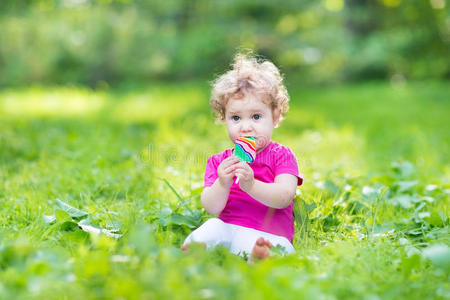 可爱的卷曲女婴在阳光明媚的夏天公园吃糖果