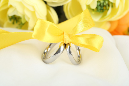 绑丝带在白色织物上的结婚戒指