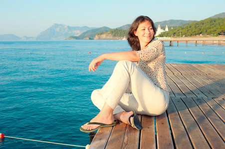 年轻的女孩正在休息在木制码头附近海