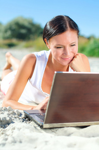 有吸引力的女人躺在海滩上的便携式计算机